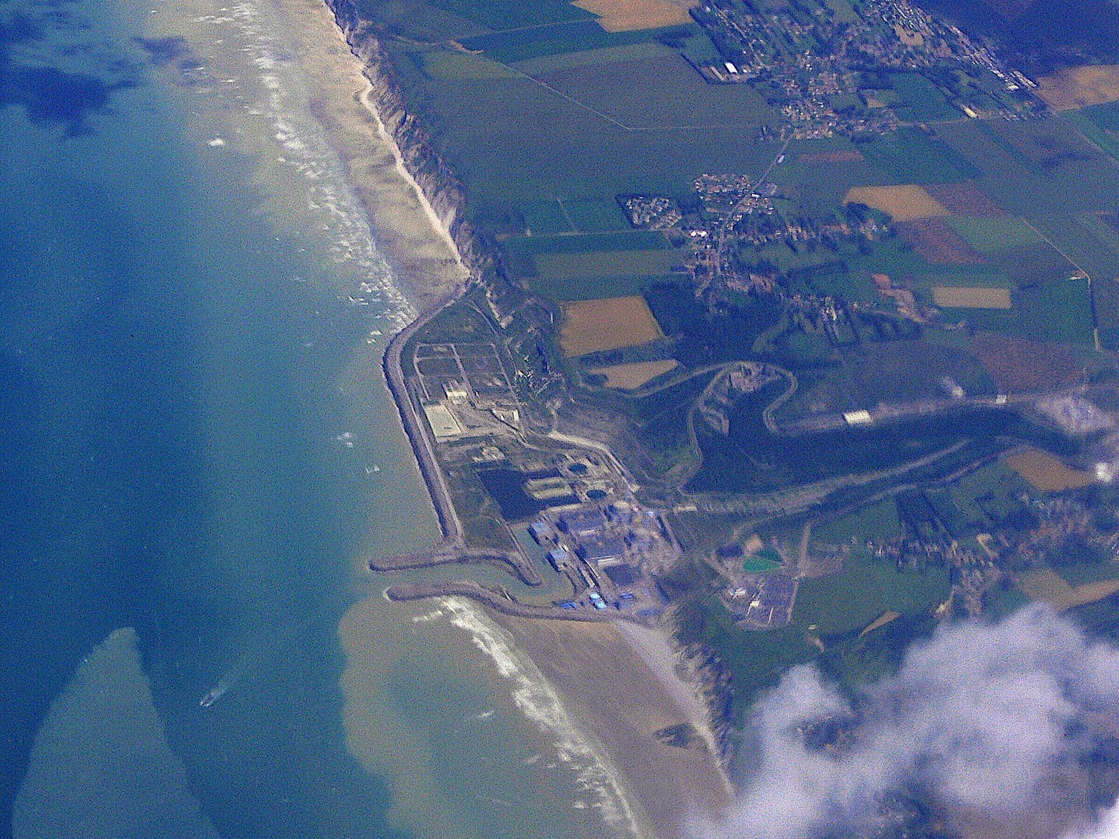 Vue aérienne d'une centrale nucléaire au bord de la mer, entourée de champs et de villages.