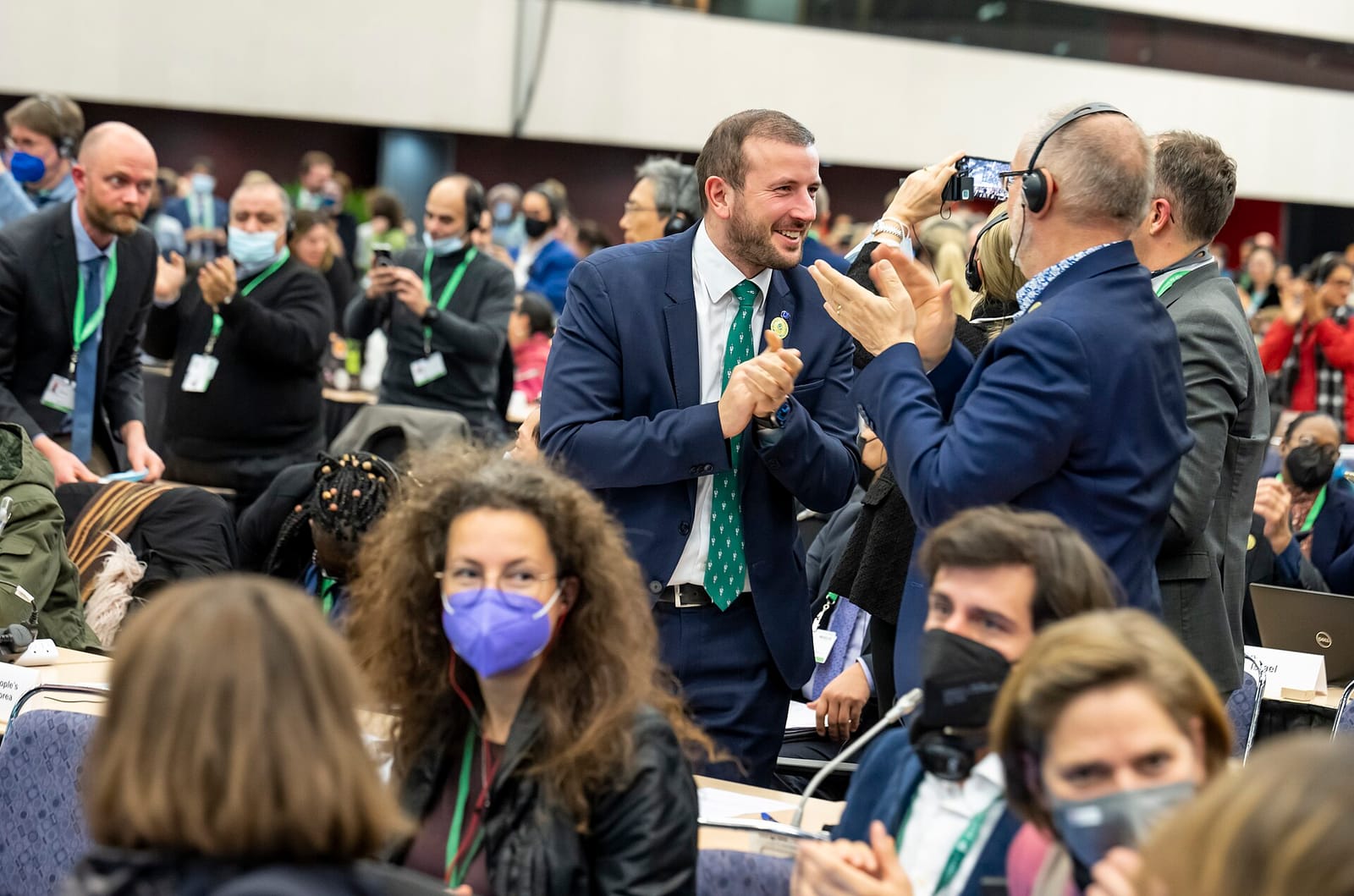 Des délégués applaudissent dans une salle de conférence, certains portant un badge et un casque de traduction.
