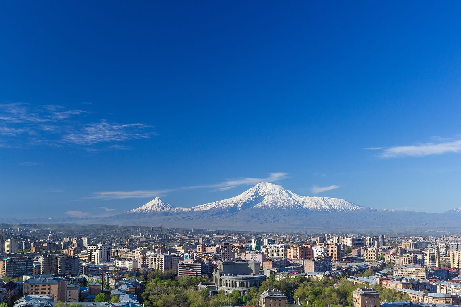 Ville d'Erevan sous un ciel bleu, avec le mont Ararat enneigé à l'horizon.