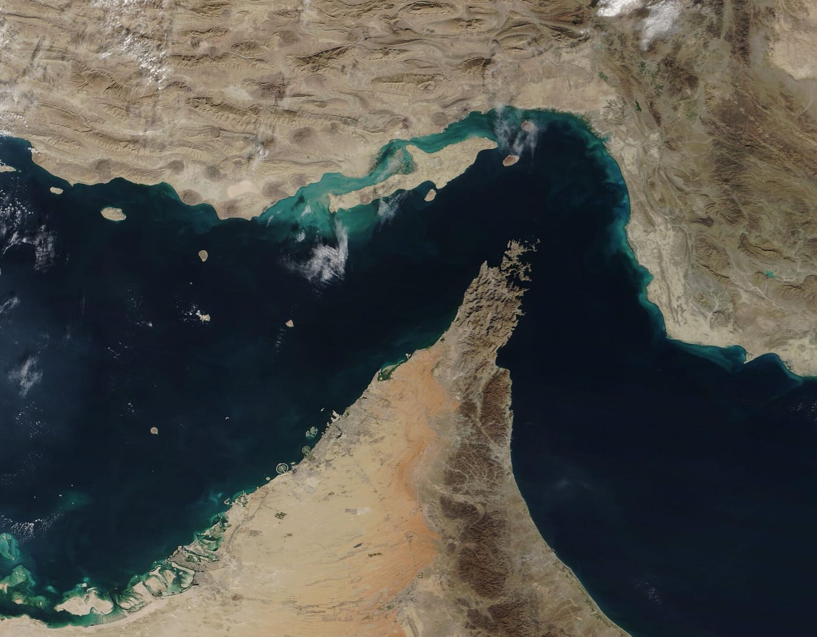 Vue satellite du détroit d'Ormuz : eaux sombres entre la côte iranienne aux terres arides au nord, avec l'île de Qeshm, et la péninsule du Musandam, au relief r