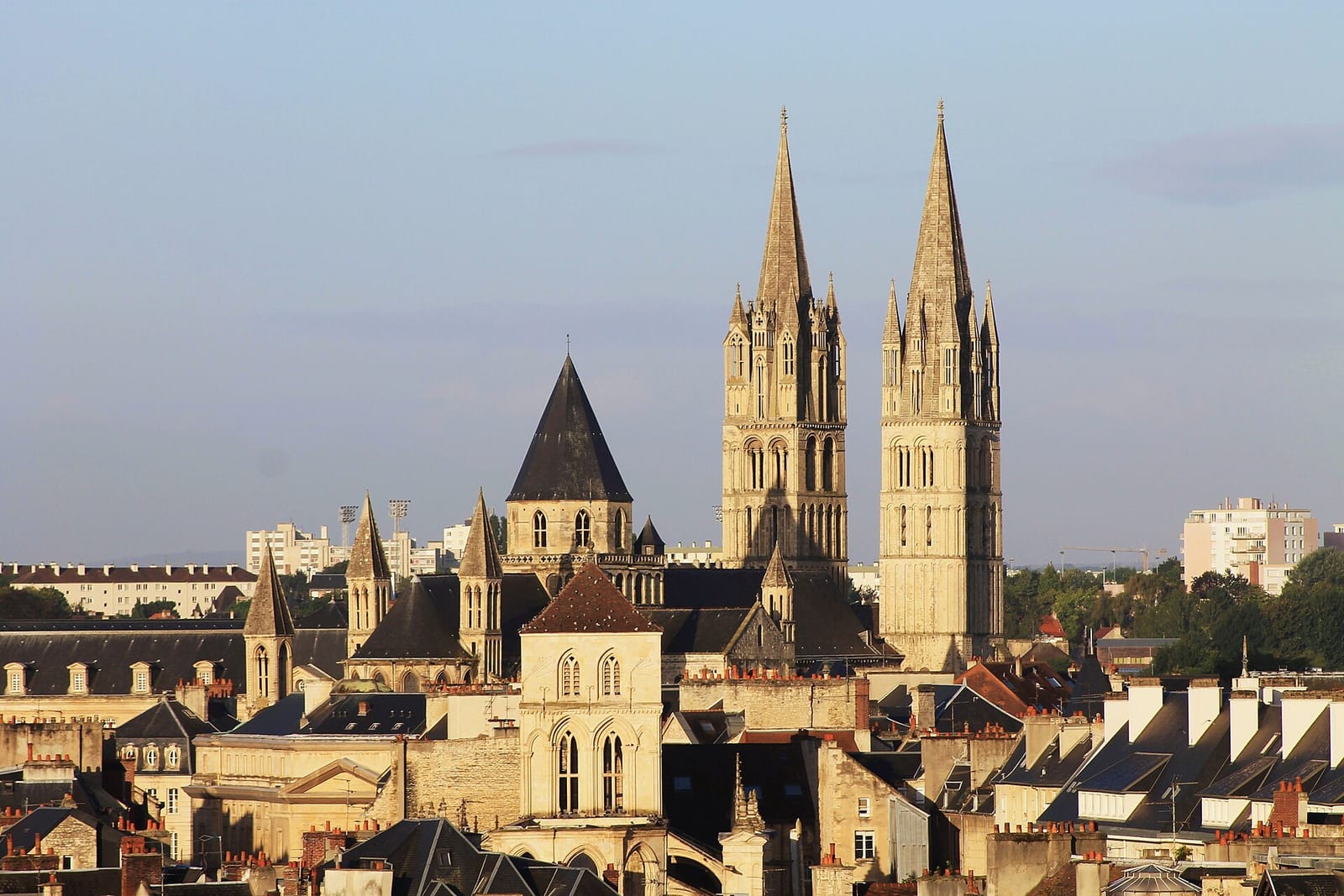 Clochers gothiques de Caen dominant les toits de la ville sous un ciel bleu clair.