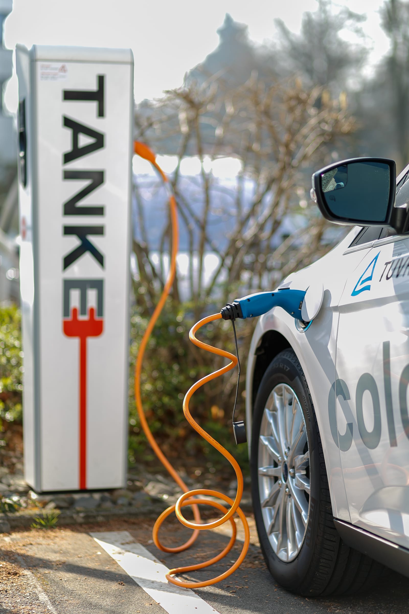 Borne blanche TANKE reliée par un câble orange à une voiture électrique blanche.