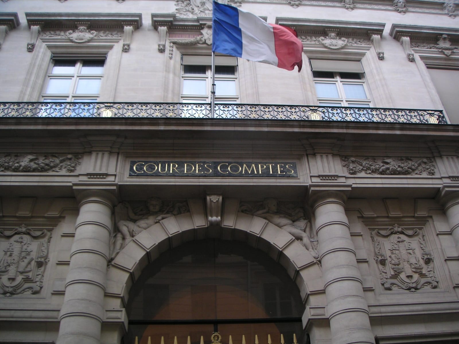 Façade de pierre de la Cour des comptes avec son inscription, un drapeau tricolore et une grille d'entrée en arrière-plan.